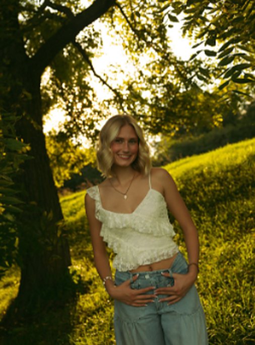 A senior girl in a white top leaning against a tree in golden light